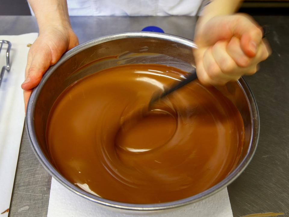 hands stir a bowl of liquid chocolate