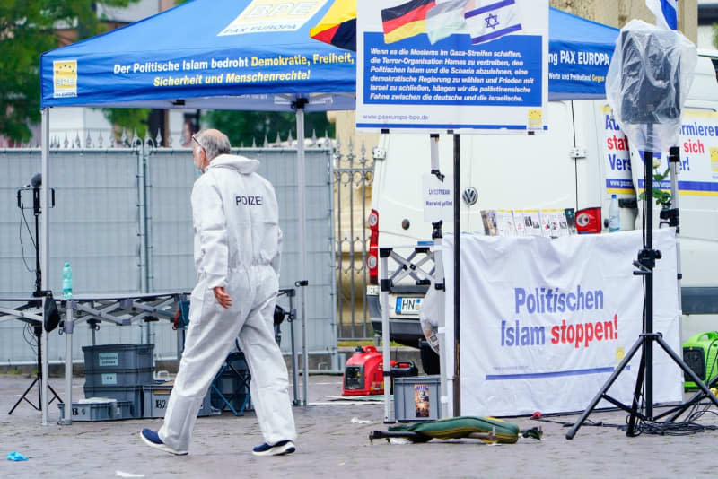 A forensics officer walks past a market square stall where a knife-wielding attacker who injured several people in a market square in the southwestern German city of Mannheim has been shot by police.  Uwe Anspach/dpa