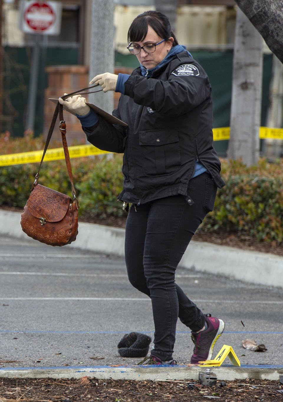 Heather Barclay, an accident investigator with the Fullerton Police Department, recovers a purse that was lodged underneath a pickup truck in the aftermath of a car accident, Sunday, Feb. 10, 2019, in Fullerton, Calif. Authorities say a suspected drunken driver was arrested after his pickup truck plowed into a crowd on a sidewalk, injuring multiple people, including some victims who were trapped under the vehicle. (Mindy Schauer/The Orange County Register via AP)