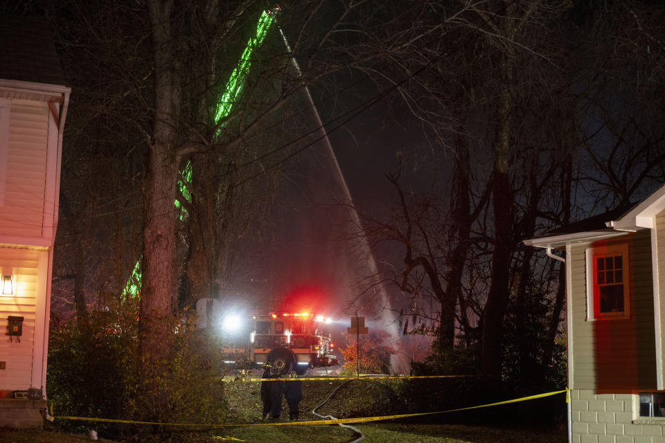 Fire and police officials walk around the scene of a house explosion as an Arlington County Fire Department ladder truck sprays water down on the remains of the building on Monday, Dec. 4, 2023, in Arlington, Va. (AP Photo/Kevin Wolf)