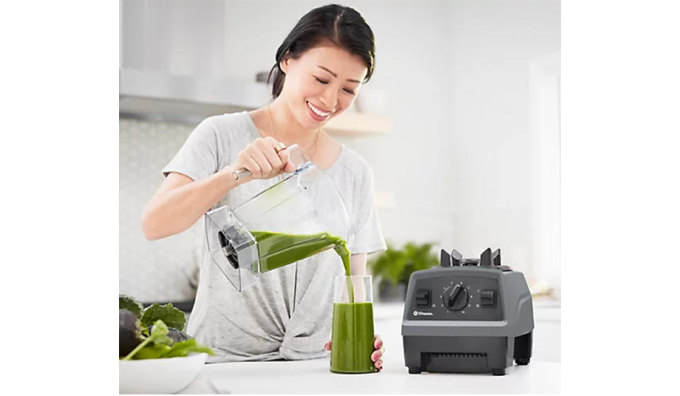 Asian woman pouring green juice from blender cup into a glass. 