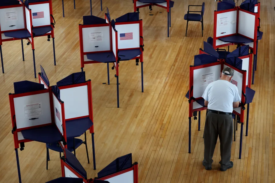 A man stands at a table as he fills out his ballot.