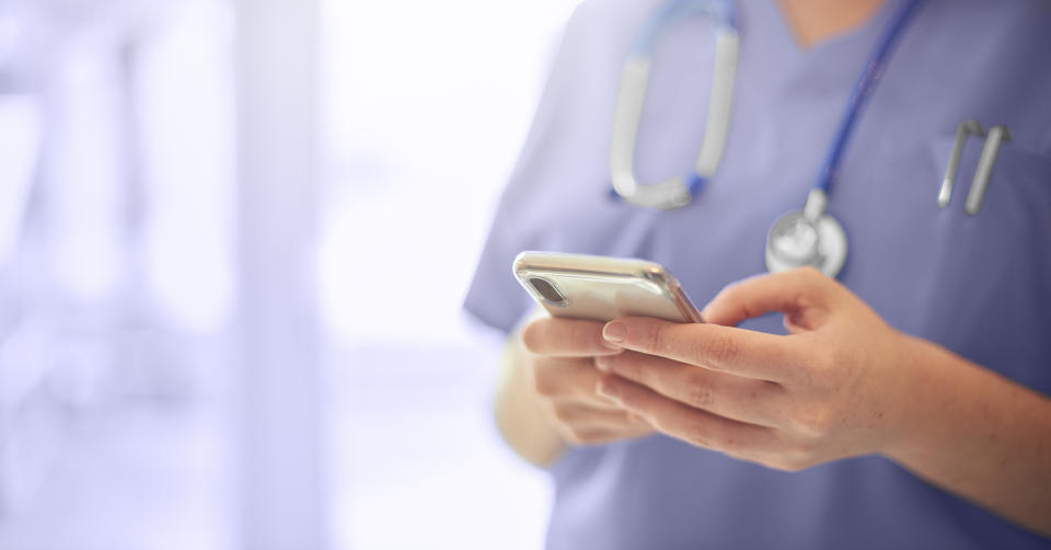 Female surgeon texting on mobile phone in hospital or surgery. She is wearing scrubs and has her stethoscope around her neck