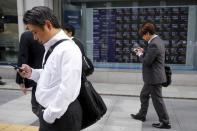 Businessmen look at their mobile phones in front of an electronic stock quotation board outside a brokerage in Tokyo, Japan, October 23, 2015. REUTERS/Toru Hanai