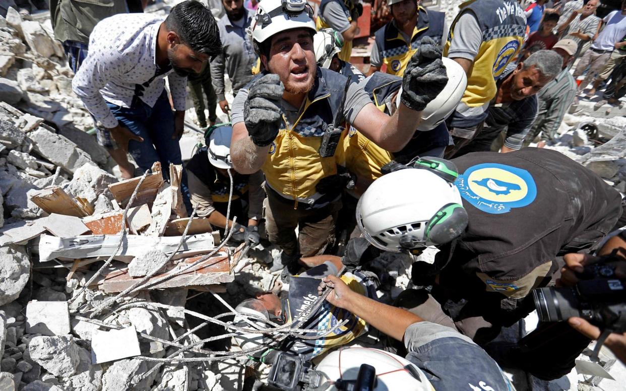 Members of the Syrian civil defence, known as the White Helmets, pull out an injured Syrian child from under the rubble following a reported Russian air strike - AFP