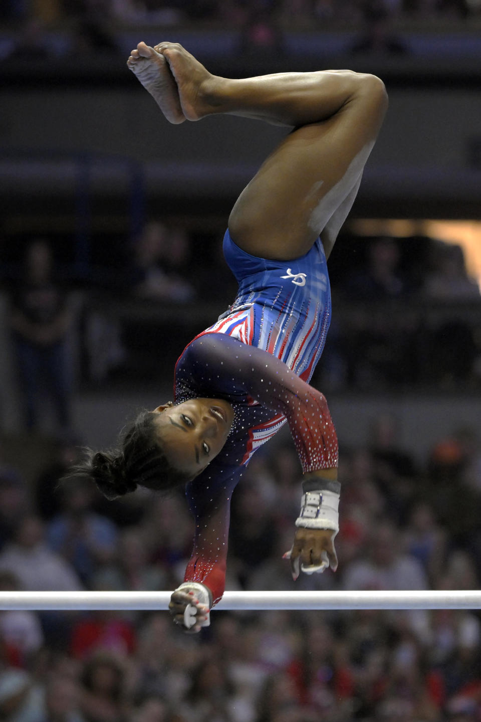 Simone Biles performs a handstand on uneven bars during a gymnastics competition, wearing a leotard with starry details