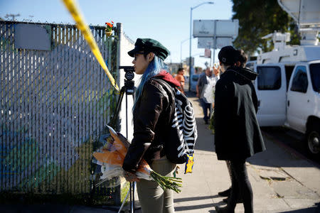 A woman carrying flowers looks toward the site of an overnight warehouse fire where a fire broke out during an electronic dance party, resulting in at least nine deaths and many unaccounted for in the Fruitvale district of Oakland, California, U.S. December 3, 2016. REUTERS/Stephen Lam