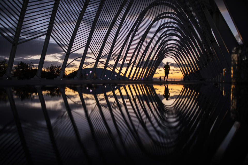 A man runs on a walkway of steel vaults, called the Agora, at the Athens Olympic Stadium complex as the sun sets, on Friday, Nov. 20, 2020. The government imposed a second lockdown nationwide on Nov. 7, expanding regional restrictions, following a dramatic surge in COVID-19 cases (AP Photo/Petros Giannakouris)