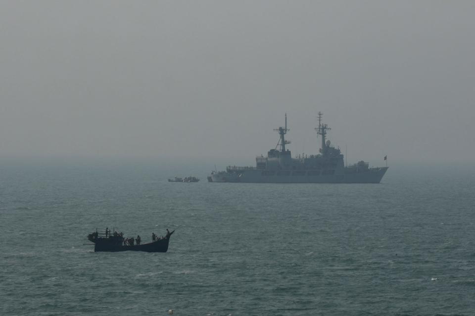 A fishing boat sails pass a Bangladesh Navy vessel