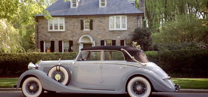 A nice, antique car in front of a large home.