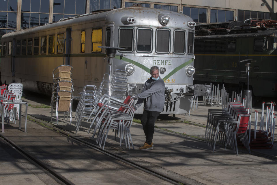 A bar worker sets out tables and chairs in a terrace bar outside an old train station which is currently a railway museum, in Madrid, Spain, Sunday, Feb. 14, 2021. Several central Spanish regions including Madrid have announced some easing of curfews and restrictions on bar and restaurants despite warnings to keep a high alert despite a slowing curve of the Coronavirus contagion. (AP Photo/Paul White)