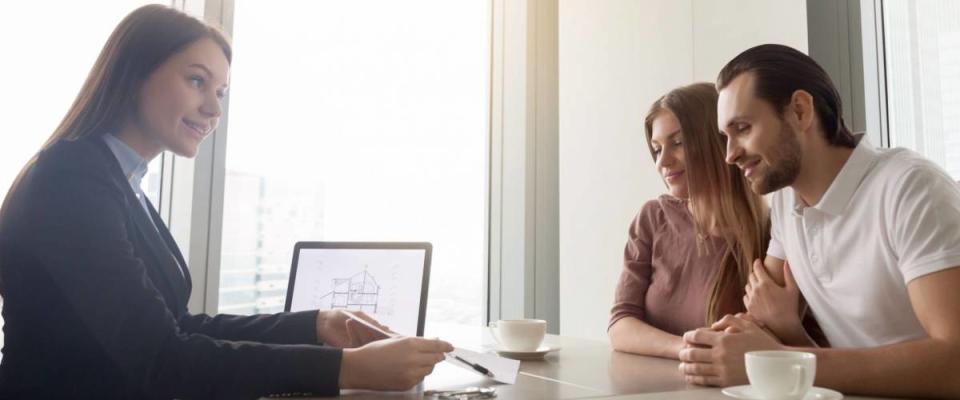 Female realtor meeting with young couple in real estate agency office.