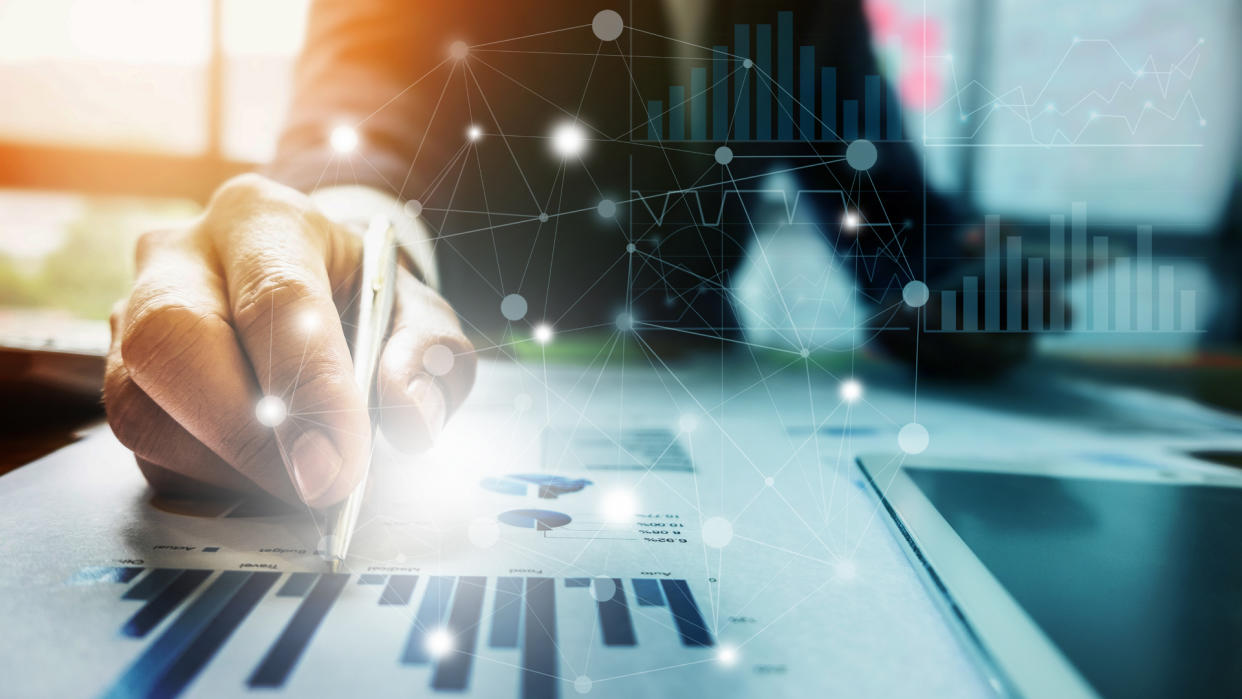 Close up Businessman hand holding pen and pointing at financial paperwork with financial network diagram.