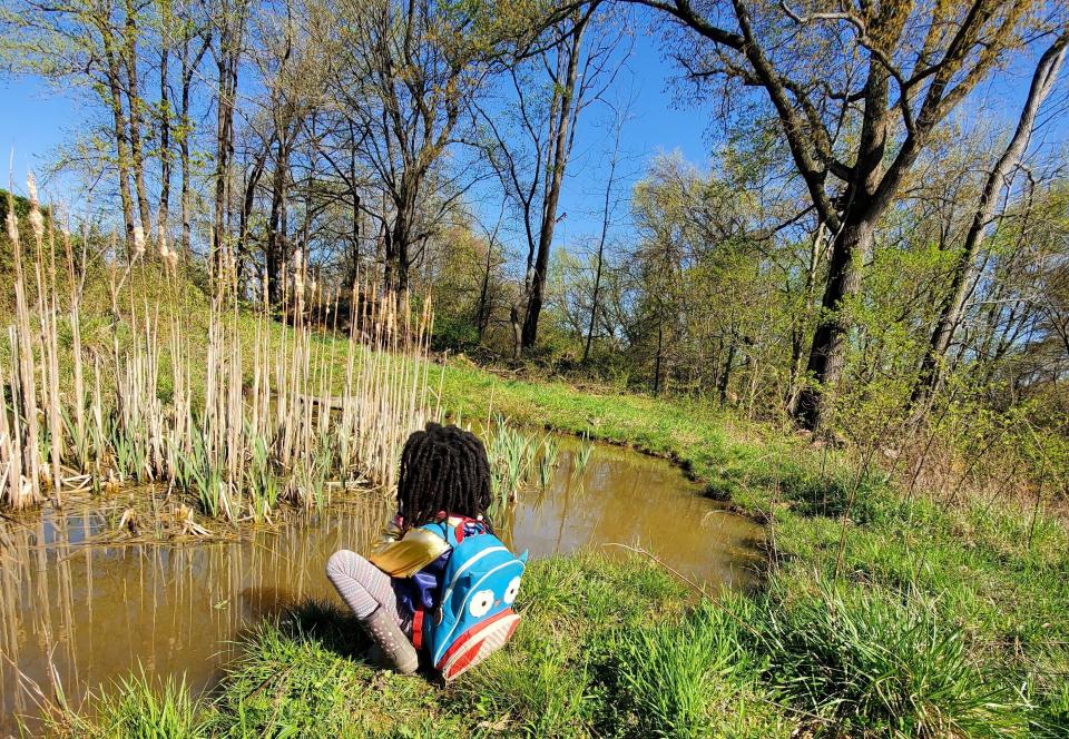 A child sits next to a pond filled with wildlife at BLISS Meadows in Baltimore. (Photo: Atiya Wells)