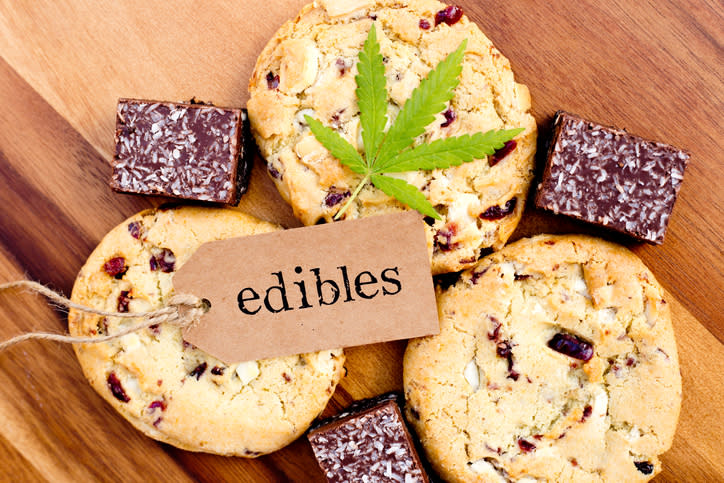 A cannabis leaf and a tag saying "edibles" lying on top of a few cookies and brownies sitting on a wood surface. 