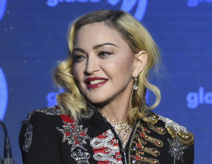 Madonna in a bejeweled black jacket looking over her right shoulder and smiling