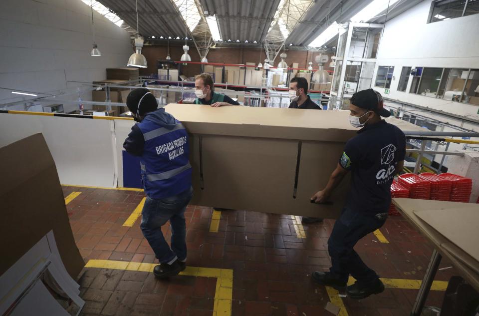 Workers at a company that designs packaging for product displays carry a box containing one of their co-workers to demonstrate how their new design of a cardboard box can serve as both a hospital bed and a coffin, designed for COVID-19 patients, in Bogota, Colombia, Friday, May 8, 2020. Owner Rodolfo Gomez said he plans to donate the first units to Colombia's Amazonas state, and that the company will sell others to small hospitals for 87 dollars. (AP Photo/Fernando Vergara)