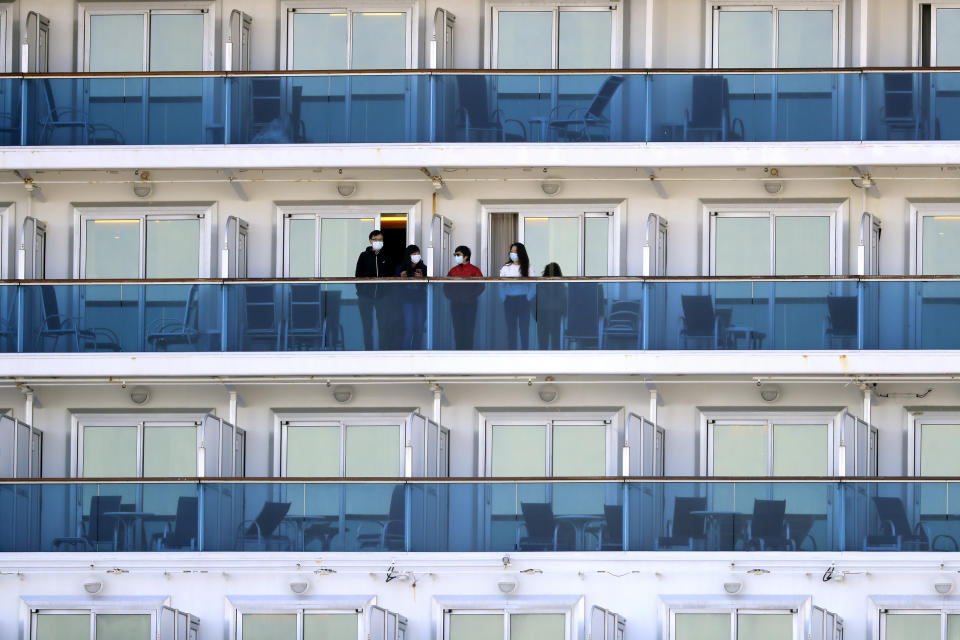 Passengers stand on the balcony of the quarantined Diamond Princess cruise ship anchored at a port in Yokohama, near Tokyo, Friday, Feb. 21, 2020. Passengers tested negative for COVID-19 started disembarking since Wednesday. (AP Photo/Eugene Hoshiko)
