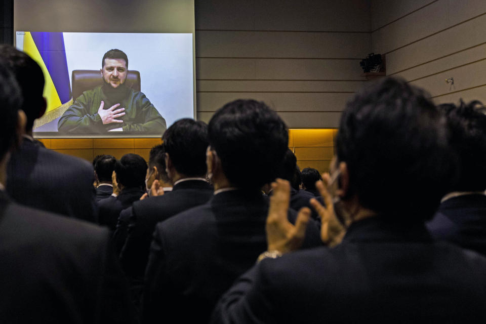 Japanese lawmakers applaud as Volodymyr Zelensky appears on a screen.