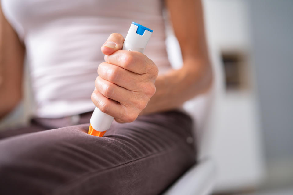 Person using an epinephrine auto-injector on their thigh for emergency treatment
