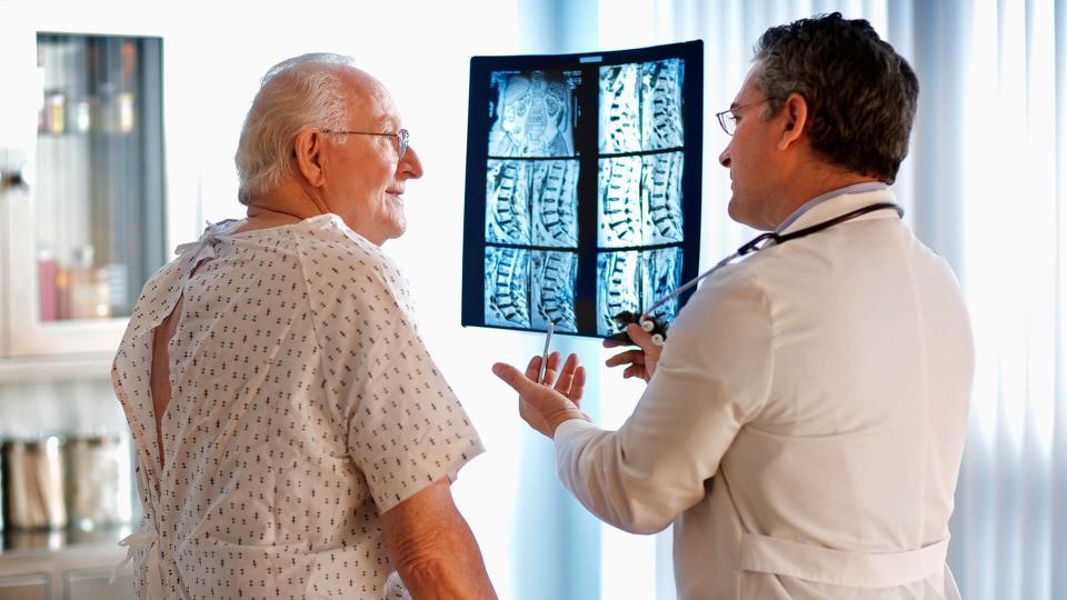 Doctor talking to senior male patient while holding up MRI.