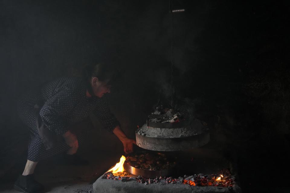Eftichia Pliakou, 77, puts the Easter lamb under the gastra, a local traditional grill, in Myrodafni village, Epirus region, northwestern Greece, on Sunday, April 24, 2022. For the first time in three years, Greeks were able to celebrate Easter without the restrictions made necessary by the coronavirus pandemic. (AP Photo/Thanassis Stavrakis)