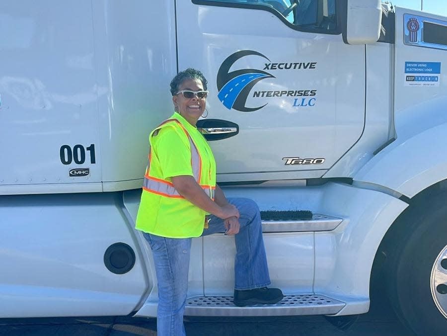 Vanita Johnson, a truck driver based in Atlanta, Georgia, poses with her white truck and a yellow visibility vest.