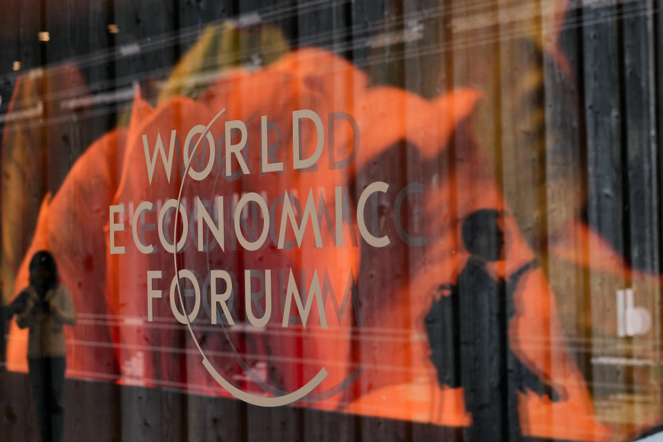 People are reflected in a window with the logo of the World Economy Forum on the last day of the forum's Annual Meeting in Davos, Switzerland, Friday, Jan. 19, 2024. (AP Photo/Markus Schreiber)