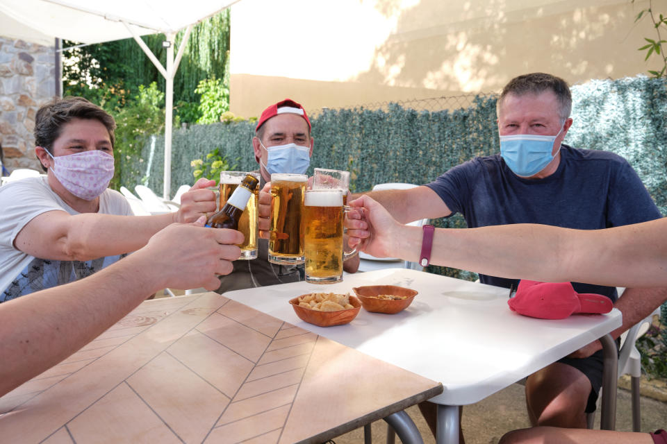 People with face masks cheering with beers in a bar. New normality in bars concept.