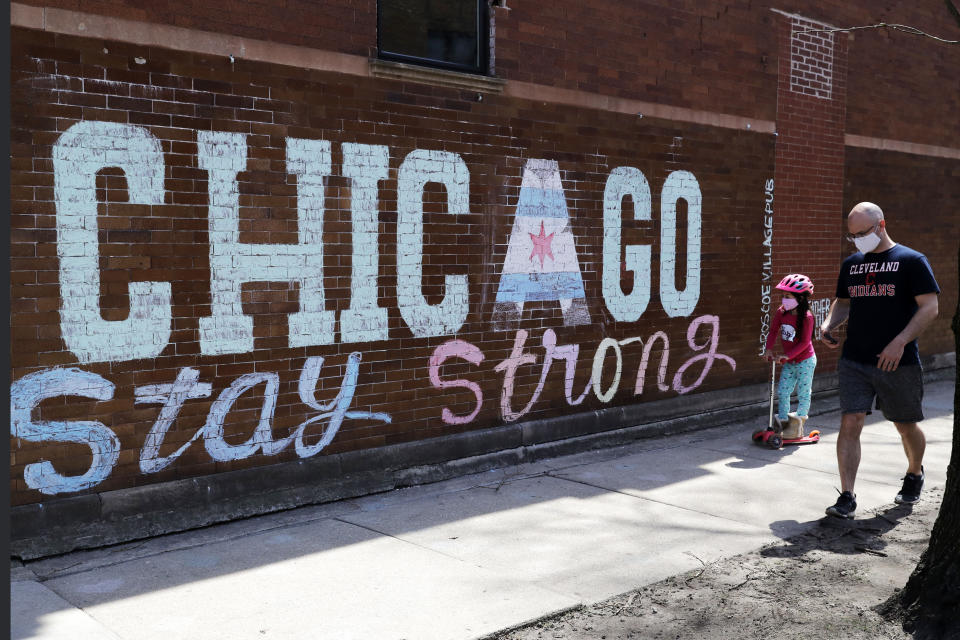 A man and child wearing protective masks pass an encouraging message 'Chicago Stay Strong,' chalked outside on a Roscoe Village neighborhood pub by artist Heather Gentile Collins, while people continue to contract COVID-19 in Chicago, Saturday, April 11, 2020. (AP Photo/Nam Y. Huh)