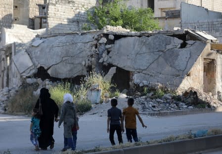 People walk near rubble of damaged buildings in the city of Idlib