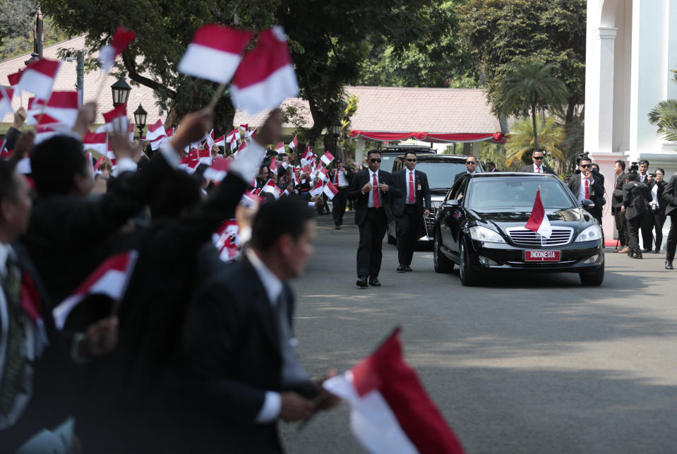 Palace staff wave Indonesian flags as the motorcade carrying President Joko Widodo leaves Merdeka Palace for the parliament building for his inauguration ceremony in Jakarta, Indonesia, Sunday, Oct. 20, 2019. The country's popular president who rose from poverty and pledged to champion democracy, fight entrenched corruption and modernize the world's most populous Muslim-majority nation is to be sworn in for his final five-year term with a pledge to take bolder actions. (AP Photo/Dita Alangkara)