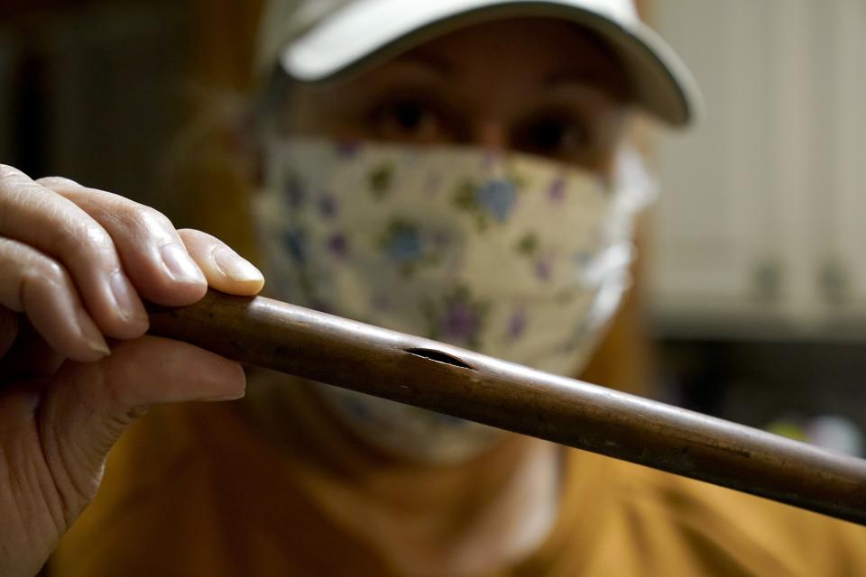 CORRECTS SPELLING OF LAST NAME TO VALERIO, NOT VALERIA - Homeowner Nora Espinoza holds a piece of the broken pipe removed by handyman Roberto Valerio on Saturday, Feb. 20, 2021 in Dallas. Espinoza's home suffered multiple pipe breaks after winter weather brought in freezing temperatures last week. (AP Photo/Tony Gutierrez)