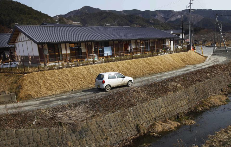 In this Tuesday, March 4, 2014, car drives past a housing complex, in Otsuchi, Iwate Prefecture, northeastern Japan. Some resettle projects have been purpose built to suit the region, like this 70 home complex that resembles a movie set from decades past, with wooden, traditional style row houses sitting on a rise above a river. (AP Photo/Junji Kurokawa)