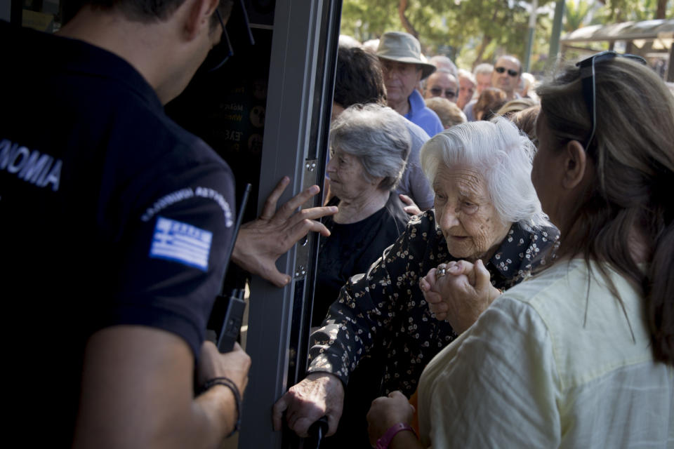 <p> Un policía griego abre la puerta de un banco para permitir que una anciana pueda ingresar  y retire un máximo de 120 euros por semana. AP