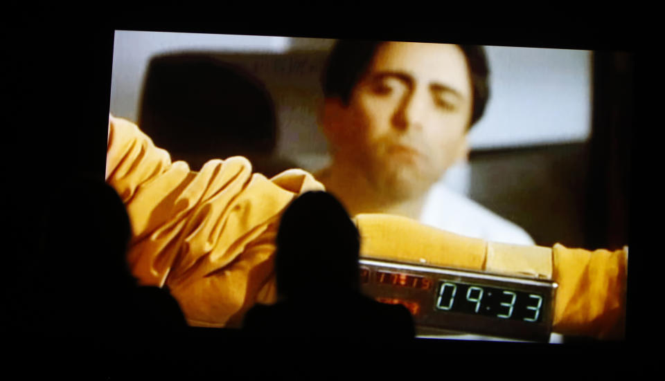 People watch a section of the 24 hour video installation by Christian Marclay, entitled ' The Clock' at the Tate Modern in London, Tuesday, Sept. 11, 2018. Christian Marclay's "The Clock" is both the ultimate movie, and an artwork you can set your watch by. The Swiss-American artist has edited together thousands of film clips containing clocks, watches or references to the time _ one or more for every minute of the day _ into a 24-hour video. It’s a mesmerizing patchwork that moves forward in time as it dances back and forth across film history. (AP Photo/Alastair Grant)