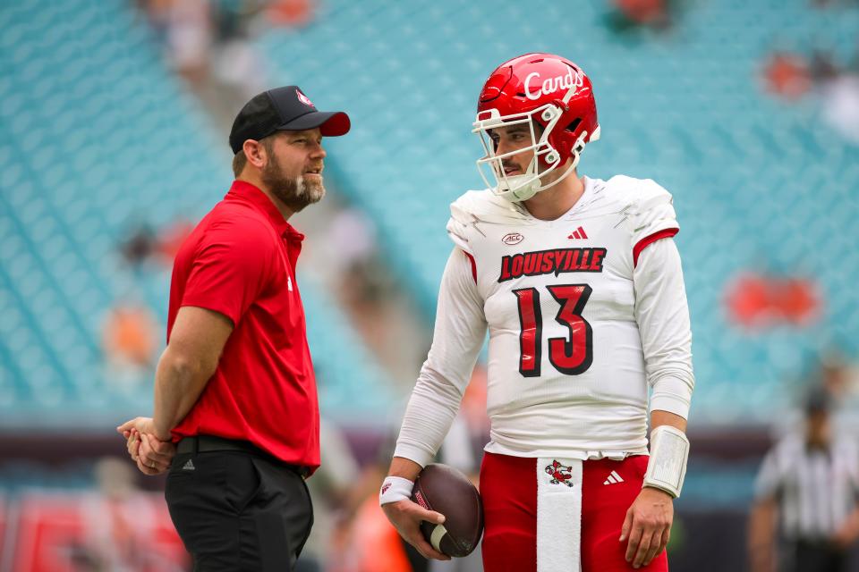 Louisville Cardinals quarterback Jack Plummer (13) talks to quarterbacks coach Brian Brohm before the game against the Miami Hurricanes at Hard Rock Stadium.