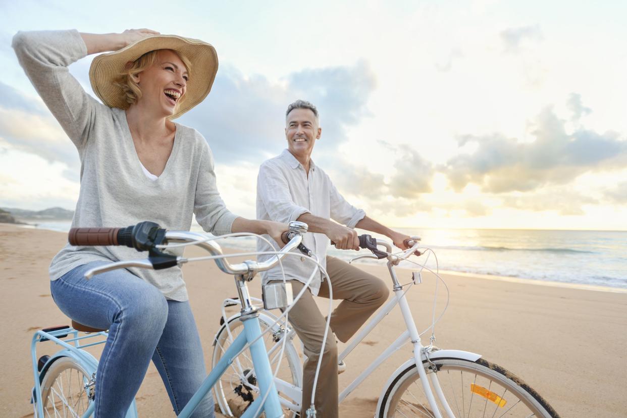 mature couple cycling on the beach at sunset or sunrise