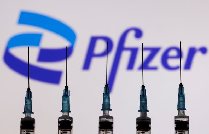 Syringes with needles are seen in front of a displayed Pfizer logo in this illustration taken