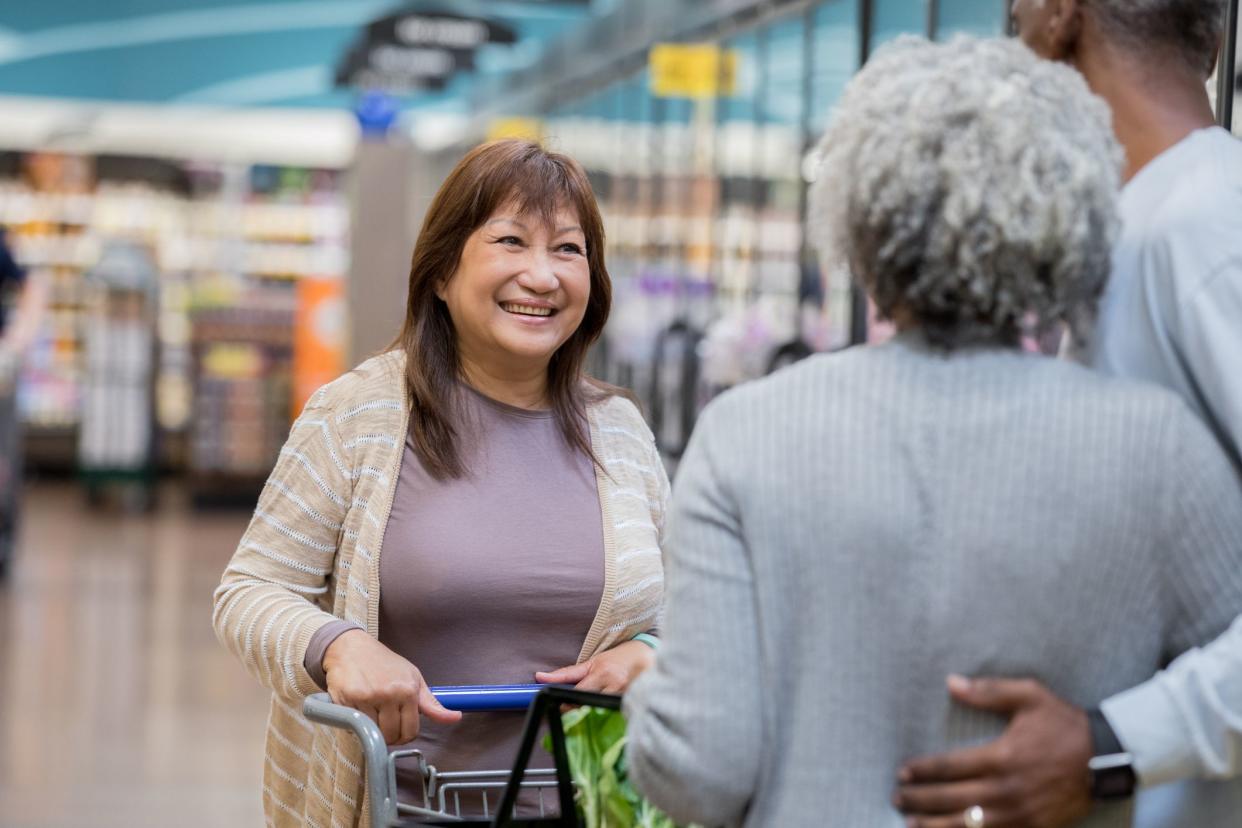 Asian senior adult female is talking to African American senior adult man and woman in grocery store