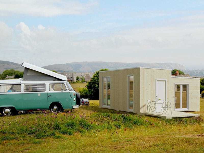 A portable off-grid Brette Haus Tiny Home rests in a field next to a VW van.