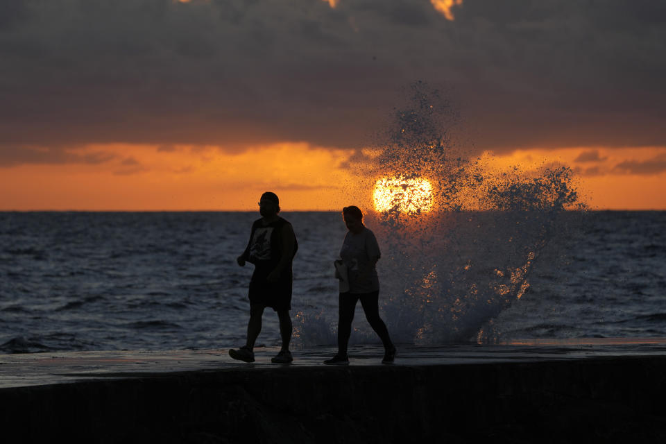 FILE - The sun rises above the Atlantic Ocean as waves crash near beach goers walking along a jetty, Dec. 7, 2022, in Bal Harbour, Fla. The world's oceans have suddenly spiked much hotter and well above record levels, with scientists trying to figure out what it means and whether it forecasts a surge in atmospheric warming. (AP Photo/Wilfredo Lee, File)