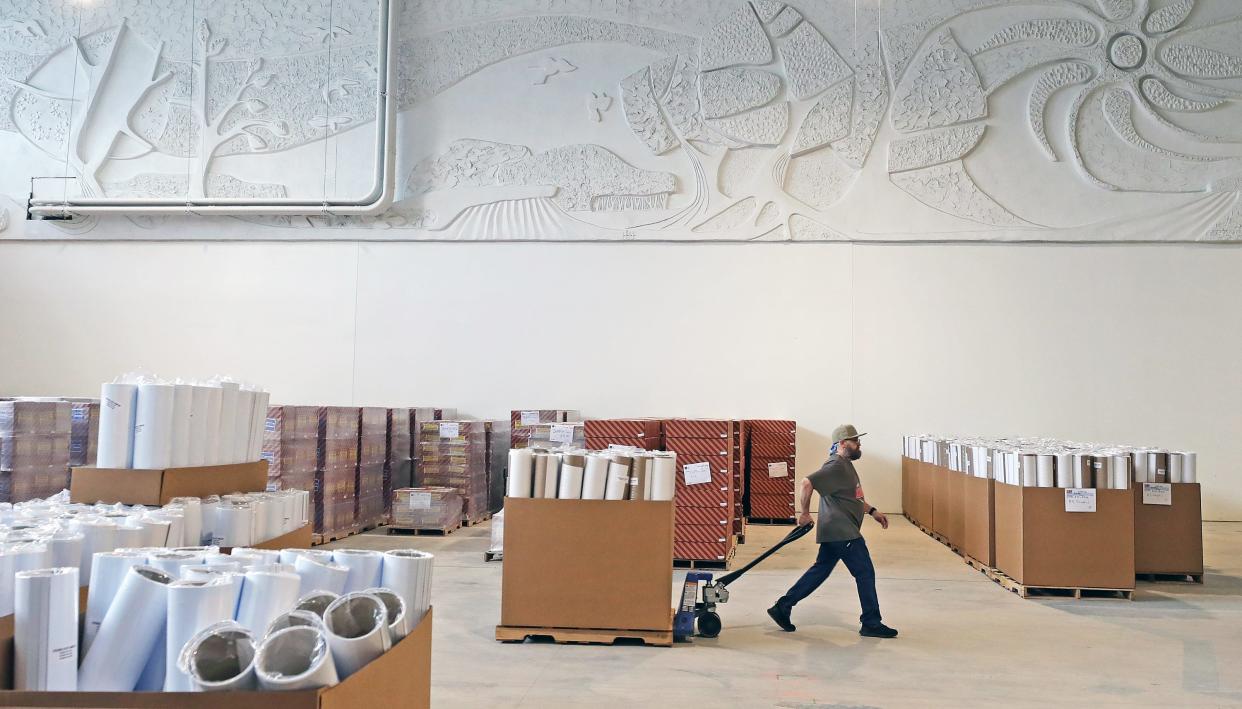 An OnQ Solutions worker prepares kits for orders under a section of a 218-foot-long mural by Cleveland artist Brian J. Plesmid titled "The Four Seasons" that shoppers once passed by on their way to JCPenney when the space was part of the Chapel Hill Mall.