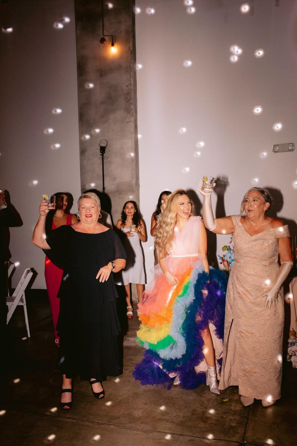 A bride in a rainbow, tulle dress stands with her wedding guests.