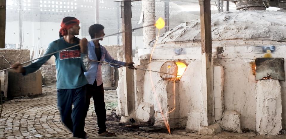 Man carries molten glass to another part of the factory