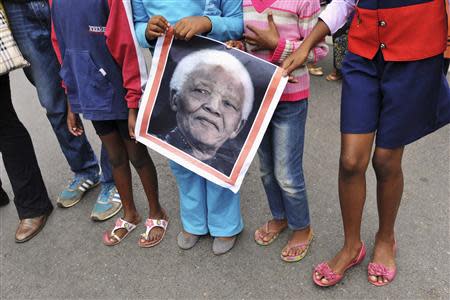 Children hold a poster of former South African President Nelson Mandela during a gathering of mourners on Vilakazi Street in Soweto, where Mandela resided when he lived in the township, December 6, 2013. REUTERS/Ihsaan Haffejee