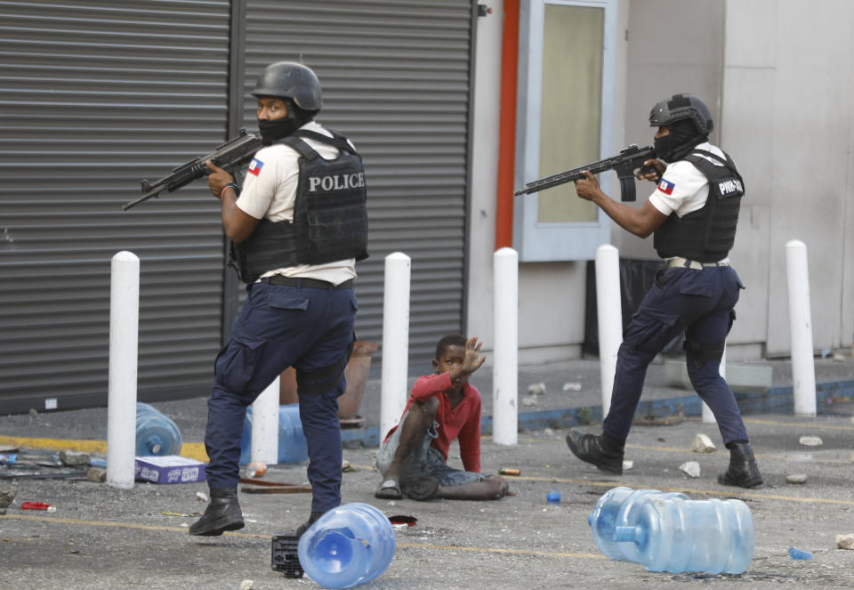 A child holds his arm up protectively as police prepare to enter a vandalized grocery store, during a protest to demand the resignation of Prime Minister Ariel Henry in the Petion-Ville neighborhood of Port-au-Prince, Haiti, Tuesday, Feb. 6, 2024. (AP Photo/Odelyn Joseph)