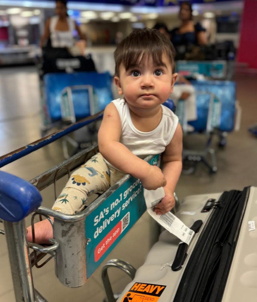 A baby on a luggage trolley in an airport