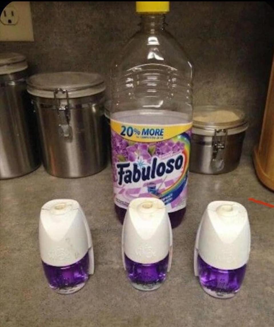 Three air fresheners filled with a purple cleaning solution in front of a large bottle of Fabuloso cleaning liquid on a kitchen counter