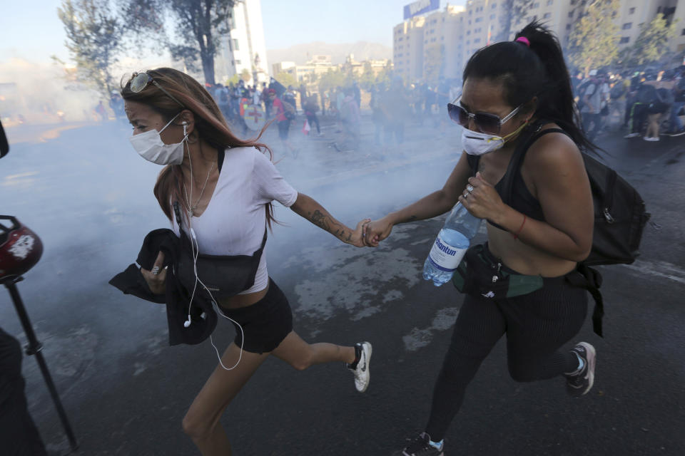 FILE - In this December 20, 2019, file photo, anti-government demonstrators run from a cloud of teargas during clashes with police in Santiago, Chile. Last year, face masks were an act of rebellion, a signature piece of clothing associated with protesters in who wore them to protect against tear gas or to conceal their identities from authorities. These same masks are now ubiquitous around the world -- worn by people from China and Iran, to Italy and America, seeking to protect against the coronavirus. The vast majority of people recover from the new virus. (AP Photo/Fernando Llano)